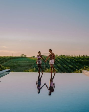 Téléchargez les photos : Couple dans un complexe de luxe piscine avec vue sur les champs de vin au coucher du soleil en Sicile Italie. - en image libre de droit