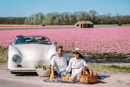 Téléchargez les photos : Couple Lisse Pays-Bas faisant un road trip avec une vieille voiture vintage dans la région des bulbes de fleurs néerlandaises avec des champs de tulipes au printemps - en image libre de droit