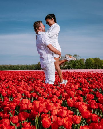 Téléchargez les photos : Deux hommes et deux femmes dans un champ de tulipes, des tulipes rouges pendant la saison printanière aux Pays-Bas en Europe, des hommes et des femmes visitent un champ de fleurs avec des tulipes - en image libre de droit