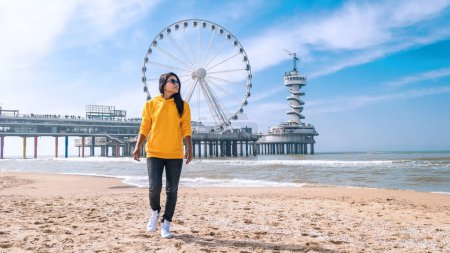 Téléchargez les photos : Femme sur la plage de Scheveningen Pays-Bas au printemps, La Grande Roue à la jetée à Scheveningen aux Pays-Bas, Jour de printemps ensoleillé à la plage de Hollande - en image libre de droit