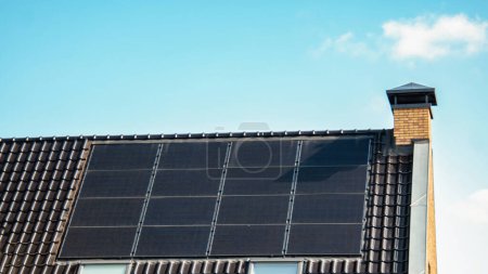 Foto de Casas de nueva construcción con paneles solares unidos en el techo contra un cielo soleado, edificios nuevos con paneles solares negros. - Imagen libre de derechos