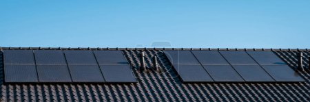 Foto de Casas de nueva construcción con paneles solares unidos en el techo contra un cielo soleado, edificios nuevos con paneles solares negros. - Imagen libre de derechos