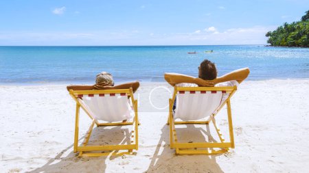 Téléchargez les photos : Hommes et femmes se détendre sur la plage dans une chaise de plage colorée, un concept de vacances à la plage avec une chaise et un ciel bleu sur l'île tropicale de Koh Kood Thaïlande. - en image libre de droit
