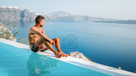 Photo for Santorini Greece Oia, young men in swim shorts relaxing in the pool looking out over the caldera of Santorini Island Greece, infinity pool, a young guy on a luxury vacation in Europe Greece - Royalty Free Image