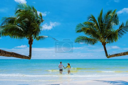 Foto de Hombres y mujeres caminando en una playa tropical con palmeras en la isla de Koh Kood Tailandia. Colgando palmeras en la playa tropical blanca con el océano azul pareja de hombres y mujeres de vacaciones - Imagen libre de derechos
