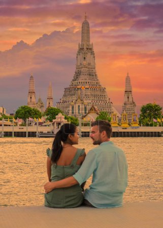 Photo for Wat Arun temple Bangkok Thailand, Temple of Dawn, a Buddhist temple alongside the Chao Phraya River.Beautiful Wat Arun at dusk evening sunset, couple Asian women and European men watching the sunset - Royalty Free Image