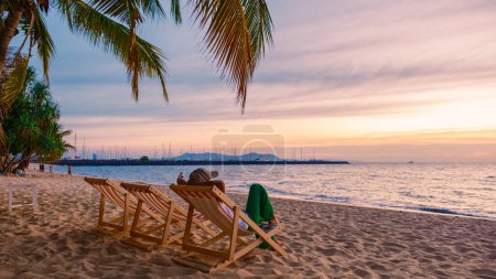 Téléchargez les photos : Asian Thai women in a beach chair watching the sunset at Na Jomtien Beach Pattaya Thailand, Palm trees at the beach. - en image libre de droit