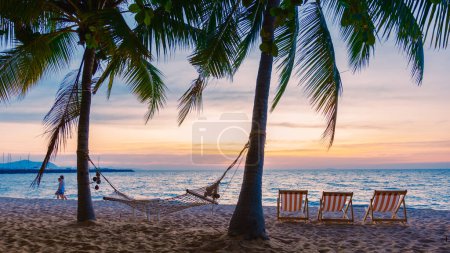 Téléchargez les photos : Hammock and beach chairs on the beach with palm trees during sunset at Na Jomtien Beach Pattaya Thailand. - en image libre de droit