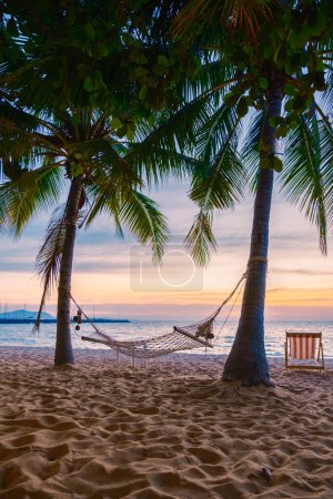 Téléchargez les photos : Hammock and beach chairs on the beach with palm trees during sunset at Na Jomtien Beach Pattaya Thailand. - en image libre de droit