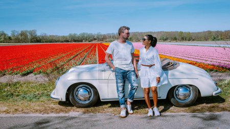 Téléchargez les photos : Couple Lisse Pays-Bas faisant un road trip avec une vieille voiture vintage dans la région des bulbes de fleurs néerlandaises avec des champs de tulipes au printemps - en image libre de droit
