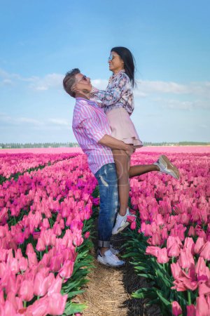 Foto de Un par de hombres y mujeres en un campo de tulipanes, tulipanes rojos durante la temporada de primavera en los Países Bajos Europa, hombres y mujeres visitan un campo de flores con tulipanes - Imagen libre de derechos