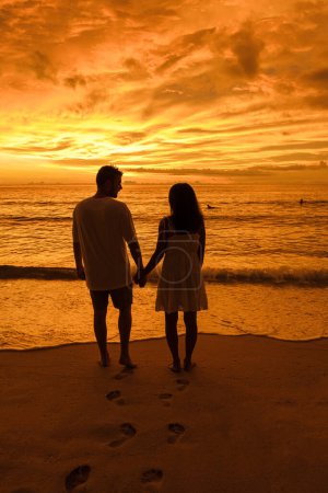 Foto de Couple watching the sunset on a beach in Phuket Thailand. Men and women during sunset on the beach with orange-red color sky - Imagen libre de derechos