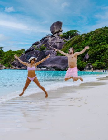 Foto de Happy young couple jump in the air on the ebach at the tropical Similan Islands in Southern Thailand, Men and women on the beach of Similan. - Imagen libre de derechos