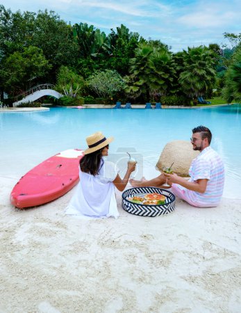 Téléchargez les photos : Couple with snacks and cocktails by the pool on a small beach in Thailand. men and women on vacation by the swimming pool - en image libre de droit
