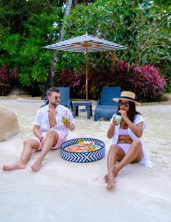 Photo for Couple with snacks and cocktails by the pool on a small beach in Thailand. men and women on vacation by the swimming pool - Royalty Free Image