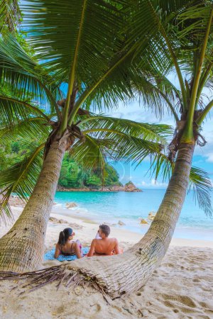 A couple of men and women relaxing on a white tropical beach with palm trees in Phuket Thailand. Banana Beach Phuket