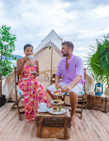 Téléchargez les photos : Couple having high tea on the beach in front of a tent, men, and women having afternoon tea at the beach in Thailand - en image libre de droit
