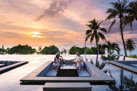 Téléchargez les photos : Couple regardant le coucher du soleil dans une piscine à débordement sur des vacances de luxe en Thaïlande, homme et femme regardant le coucher du soleil sur le bord d'une piscine en Thaïlande en vacances - en image libre de droit