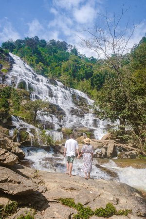 Foto de Couple visits Mae Ya Waterfall Doi Inthanon national park Thailand Chiang Mai. Asian women and caucasian men visit a waterfall - Imagen libre de derechos