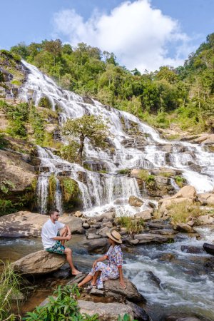 Foto de Couple visits Mae Ya Waterfall Doi Inthanon national park Thailand Chiang Mai. Asian women and caucasian men visit a waterfall - Imagen libre de derechos