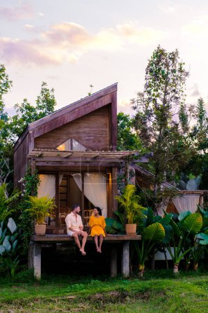 Foto de A couple of men and women at a cottage homestay in Northern Thailand Nan Province looking out over the rice paddies in Thailand, green rice fields. - Imagen libre de derechos
