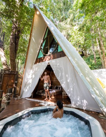 Téléchargez les photos : Couple homme et femmes dans une tente avec un jacuzzi dans la forêt tropicale de la jungle. Glamping de luxe - en image libre de droit