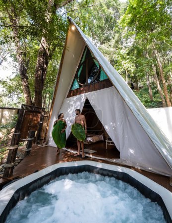 Téléchargez les photos : Couple homme et femmes dans une tente avec un jacuzzi dans la forêt tropicale de la jungle. Glamping de luxe - en image libre de droit