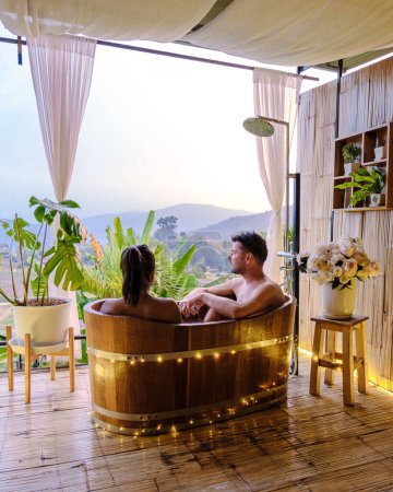 Téléchargez les photos : A couple of caucasian men and Asian women in a bathtub in the evening during sunset, a couple in a bathtub. - en image libre de droit