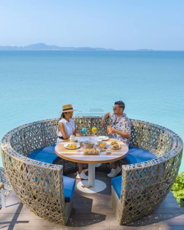 Téléchargez les photos : Couple déjeuner dans un restaurant donnant sur l'océan de Pattaya Thaïlande, homme et femme dîner dans un restaurant au bord de l'océan à Pattaya pendant l'été - en image libre de droit