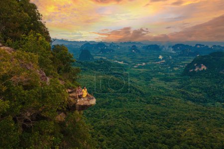 Photo for Dragon Crest mountain Krabi Thailand, a Young traveler sits on a rock that overhangs the abyss, with a beautiful landscape. Dragon Crest or Khuan Sai at Khao Ngon Nak Nature Trail in Krabi, Thailand. - Royalty Free Image