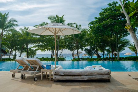 Téléchargez les photos : Beach chairs at a swimming pool at a luxury hotel, sun bed, and umbrella. - en image libre de droit