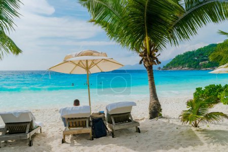 Foto de Women relaxing in a Beach chair at a tropical beach sunbed chair and umbrella and palm trees in Mahe Seychelles. - Imagen libre de derechos