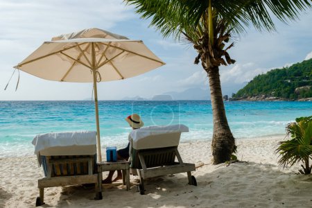 Téléchargez les photos : Women relaxing in a Beach chair at a tropical beach sunbed chair and umbrella and palm trees in Mahe Seychelles. - en image libre de droit