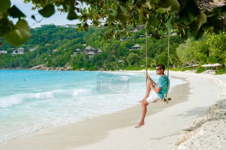 Téléchargez les photos : Young men relaxing in a swing on the beach of Mahe Tropical Seychelles Islands. - en image libre de droit