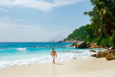 Téléchargez les photos : Young men in a swim short on a white tropical beach with palm trees Petite Anse beach Mahe Tropical Seychelles Islands. - en image libre de droit