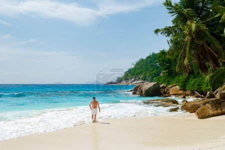 Téléchargez les photos : Young men in swim short on a white tropical beach with palm trees Petite Anse beach Mahe Tropical Seychelles Islands. - en image libre de droit