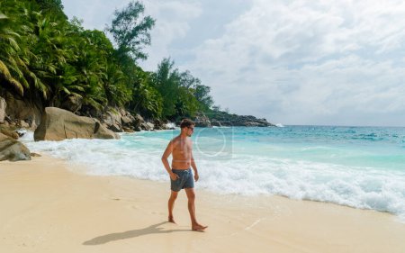 Foto de Young men in a swim short on a white tropical beach with palm trees Petite Anse beach Mahe Tropical Seychelles Islands on a sunny day - Imagen libre de derechos