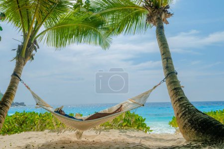 Foto de Women in a hammock under a palm tree at Petite Anse beach Mahe Tropical Seychelles Islands. - Imagen libre de derechos