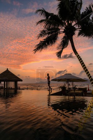Foto de Young men at a swimming pool at a luxury hotel, a Luxury swimming pool in a tropical resort, relaxing holidays. A young man during sunset by swim pool, men watching a sunset in an infinity pool - Imagen libre de derechos