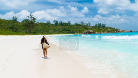 Photo for Young Asian woman with a hat walking at a tropical beach, Anse Cocos beach La Digue Seychelles Islands. - Royalty Free Image