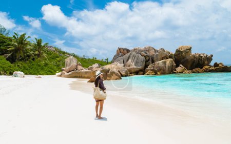 Foto de Young Asian woman with a hat walking at a tropical beach, Anse Cocos beach La Digue Seychelles Islands. - Imagen libre de derechos
