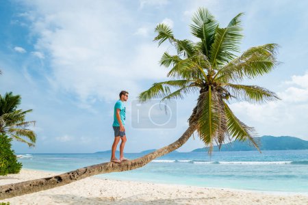 Téléchargez les photos : Young men relaxing at a palm tree on a tropical white beach at the La Digue Seychelles Islands. - en image libre de droit