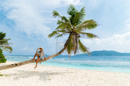 Foto de Young woman relaxing at a coconut palm tree on a white tropical beach at La Digue Seychelles Islands. - Imagen libre de derechos