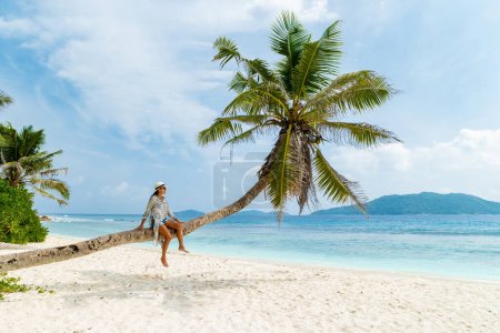 Young woman relaxing at a coconut palm tree on a white tropical beach at La Digue Seychelles Islands. 