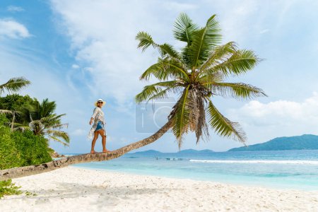 Foto de Asian woman relaxing at a coconut palm tree on a white tropical beach at La Digue Seychelles Islands. - Imagen libre de derechos
