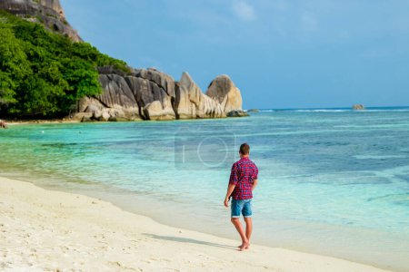 Téléchargez les photos : Young men walking at a white tropical beach Anse Source dArgent beach La Digue Seychelles Islands. - en image libre de droit