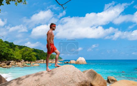 Téléchargez les photos : Young men in a swim short at Anse Lazio beach with turquoise colored ocean Praslin Seychelles Islands on a sunny day - en image libre de droit