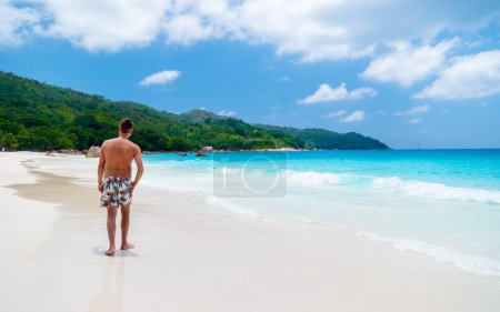 Junge Männer im Badeanzug entspannen sich am Strand von Anse Latium mit türkisfarbenem Meer auf den Seychellen.