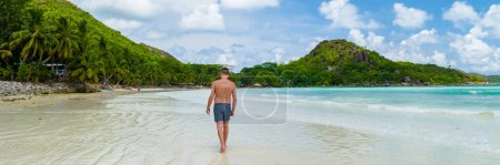 Photo for Young tanning men in swim short at a white tropical beach with turquoise colored ocean Anse Volbert beach Praslin Seychelles. - Royalty Free Image