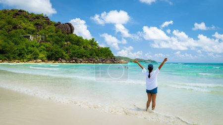 Téléchargez les photos : Jeune femme les mains en l'air sur une plage tropicale blanche avec un océan de couleur turquoise Anse Volbert plage Praslin Tropical Seychelles Islands. Plage de Cote Dor - en image libre de droit